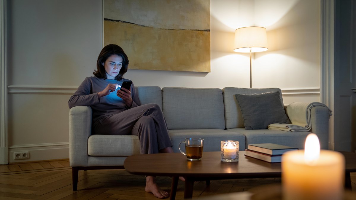 Frau hält abends ihr Handy und kämpft mit der emotionalen Abhängigkeit nach der Trennung